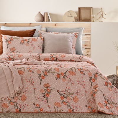 Cama com colcha floral cor de rosa, almofadas cinza e castanho, manta rosa, e cabeceira de madeira