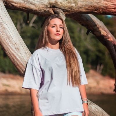 Mulher a usar t-shirt branca e calções de ganga junto a troncos de madeira perto de um lago.
