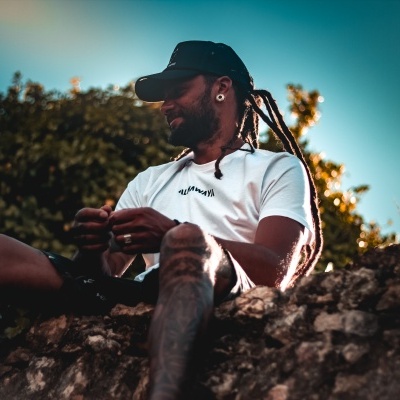 Homem com t-shirt branca e boné sentado numa rocha ao ar livre