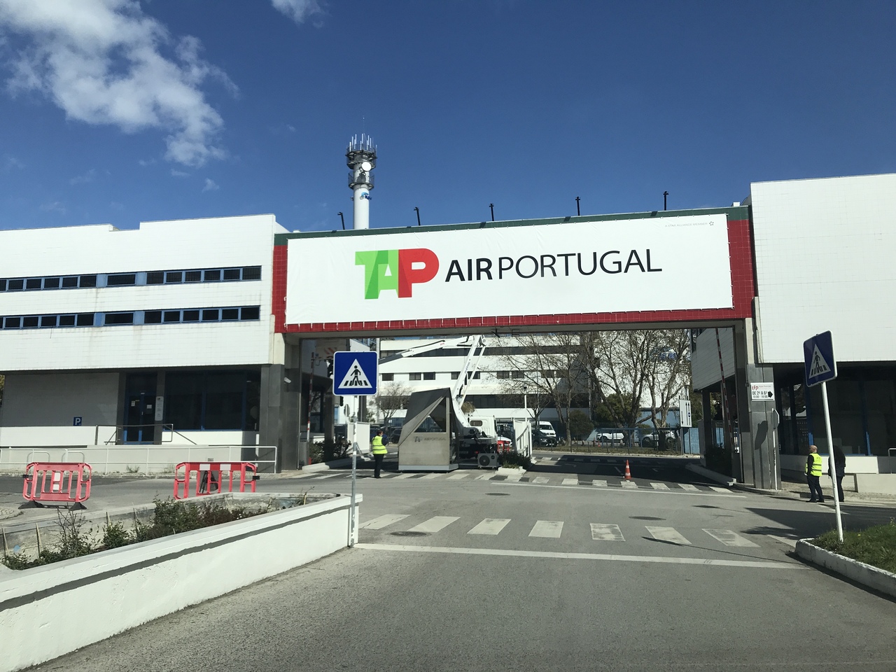 Lona Premium Entrada de acesso com letreiro TAP AIR PORTUGAL e edifícios ao fundo