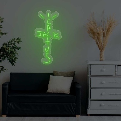 Neon verde em forma de cacto iluminado na parede acima de sofá preto entre planta e cómoda branca