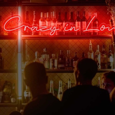 Bar com prateleiras de garrafas e letreiro néon vermelho 'Crazy in Love'