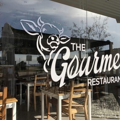 Montra de restaurante com logotipo THE Gourmet RESTAURANT e desenho de vaca
