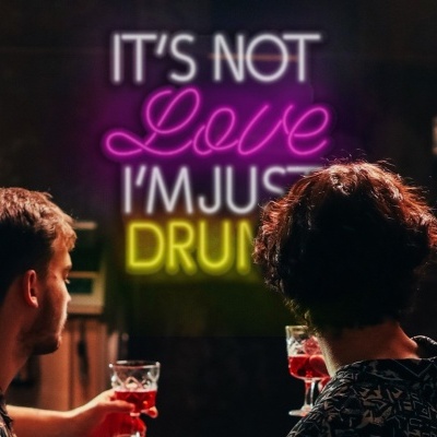 Duas pessoas num bar com letreiro néon IT'S NOT Love I'M JUST DRUNK