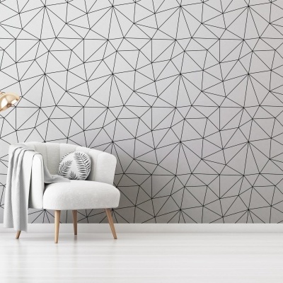 Poltrona cinza claro com almofada decorativa e candeeiro dourado junto a parede com padrão geométrico cinza