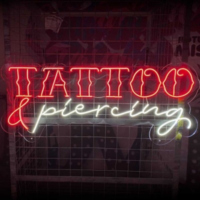 Sinal de neon com as palavras TATTOO em vermelho e piercing em branco sobre uma grade metálica