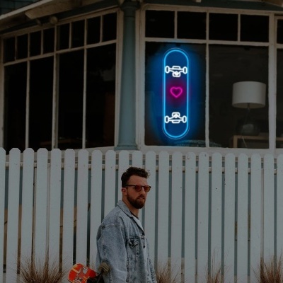 Placa de néon azul com ícones e coração vermelho numa parede branca com vedação em madeira e homem em primeiro plano