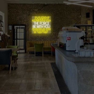 Interior de café com paredes de tijolo, cadeiras coloridas e letreiro luminoso amarelo