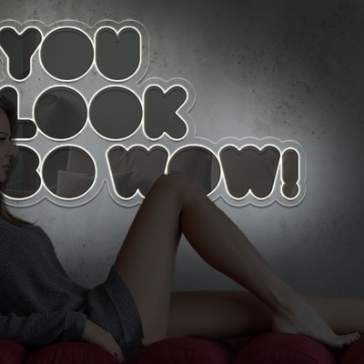 Mulher sentada em cadeira vermelha junto a luz de néon com frase motivacional.