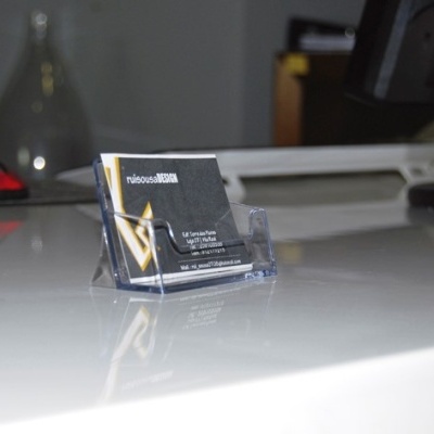 Cartão de visita num suporte plástico sobre mesa branca com rato de computador e ecrã ao fundo