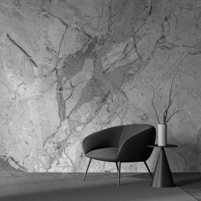 Cadeira preta estofada, mesa lateral preta com vaso branco e ramos, parede de mármore cinzento