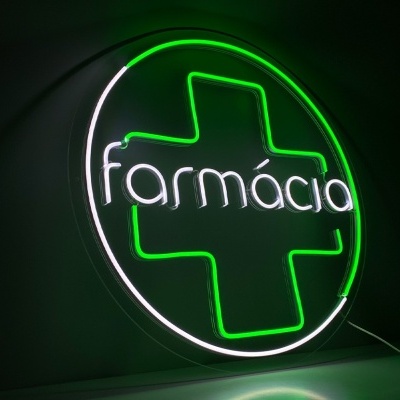 Placa de néon com cruz verde e palavra 'farmácia' iluminada