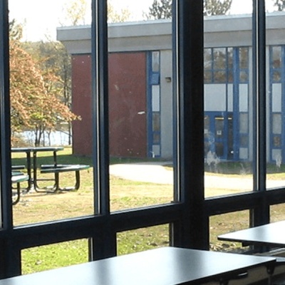 Vista exterior de café ou refeitório com mesas e bancos através de janelas de metal
