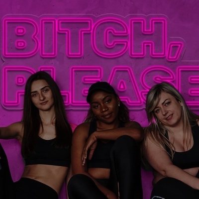 Três mulheres em roupa desportiva preta posam sentadas com um letreiro rosa LED atrás