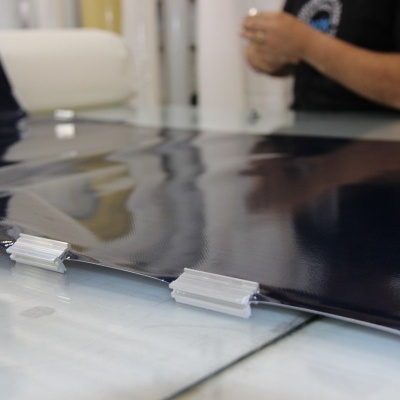 Folha de plástico azul escuro brilhante em superfície com clips transparentes, pessoa ao fundo