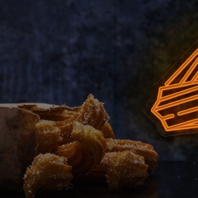 Churros dourados a sair de saco de papel castanho com logótipo neon laranja no fundo