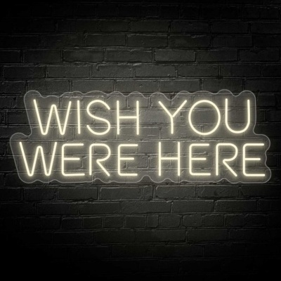 Letreiro em néon com a frase 'WISH YOU WERE HERE' numa parede de tijolos pretos