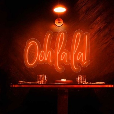 Interior acolhedor com mesa, cadeiras pretas, iluminação laranja e letreiro de néon 'Ooh la la!'