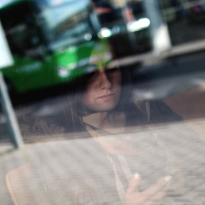 Reflexo no vidro de autocarro verde e mulher com dispositivo móvel