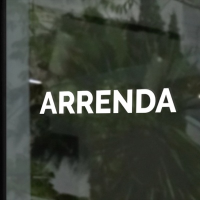Vidro com texto branco ARRENDA e reflexos de planta e luzes no teto