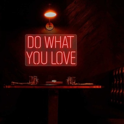 Placa de néon vermelha DO WHAT YOU LOVE numa parede escura entre bancos de pele preta e mesa de madeira