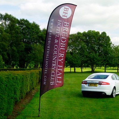 Bandeira promocional ao lado de carro branco em relvado com árvores ao fundo