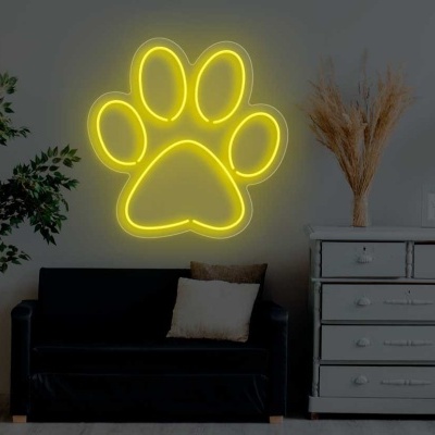 Neon amarelo em forma de pata de animal acima de sofá preto e cómoda cinzenta