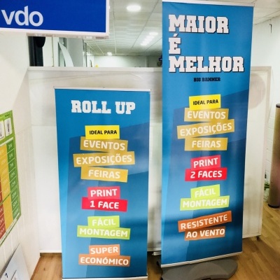 Dois roll ups publicitários azuis com texto sobre características de impressão e montagem, dentro de um escritório.