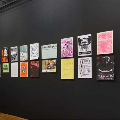 Parede preta com 20 posters artísticos variados expostos em sequência num ambiente interior