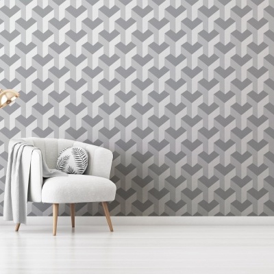 Cadeira cinza claro com almofada e manta junto a candeeiro dourado numa sala com parede geométrica