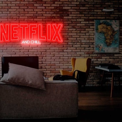 Sala com sofá cinzento, poltrona amarela e letreiro néon NETFLIX AND CHILL