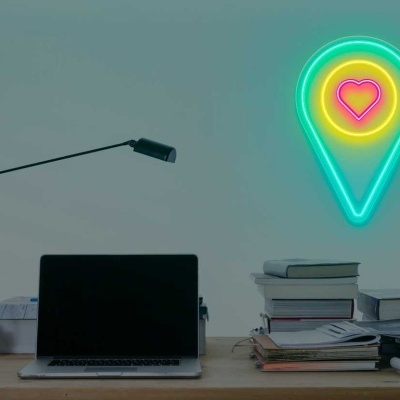 Escritório minimalista com mesa, portátil e decoração luminosa em forma de marcador de mapa com coração