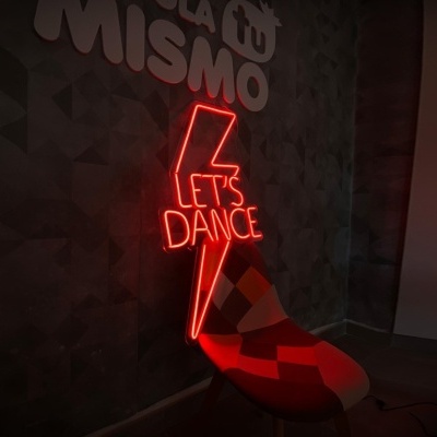 Neon vermelho com texto LET'S DANCE na parede e cadeira colorida ao lado