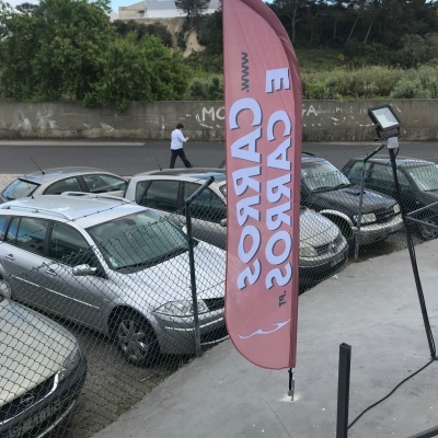 Faixa vermelha com texto 'CARROS' branco em estacionamento ao ar livre com vários carros