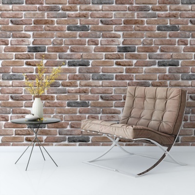 Cadeira de pele castanha e mesa lateral preta com vaso branco e flores amarelas em parede de tijolos.