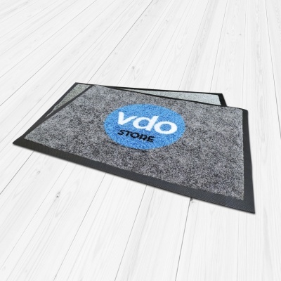 Tapete cinzento com logótipo azul e preto sobre chão de madeira clara