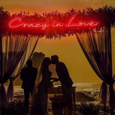 Estrutura decorativa com cortinas brancas, luz néon 'Crazy in Love' na praia ao pôr do sol