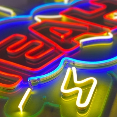 Placa de neon colorida com texto e símbolos iluminados sobre fundo escuro