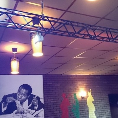 Candeeiros de metal pendurados em teto, fotografia em preto e branco e silhuetas coloridas numa parede de tijolo