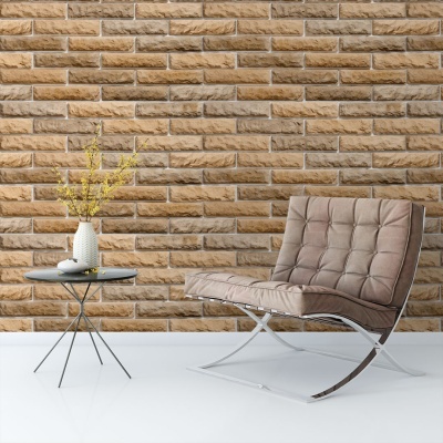 Poltrona bege acolchoada ao lado de mesa preta com vaso e flores, frente a parede de tijolos