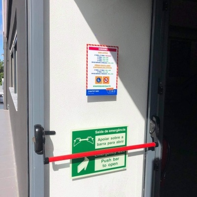 Porta de emergência branca com barra vermelha e sinais verdes de instrução