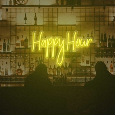 Bar com iluminação amarela em néon com a frase Happy Hour e garrafas em prateleiras
