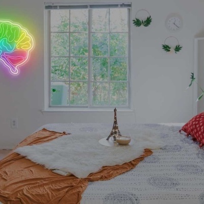 Quarto com cama com almofadas e manta, mural de cérebro neon colorido na parede branca e planta ao lado