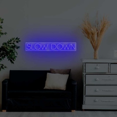 Sala com sofá preto, cómoda cinzenta e sinal luminoso azul com texto SLOW DOWN