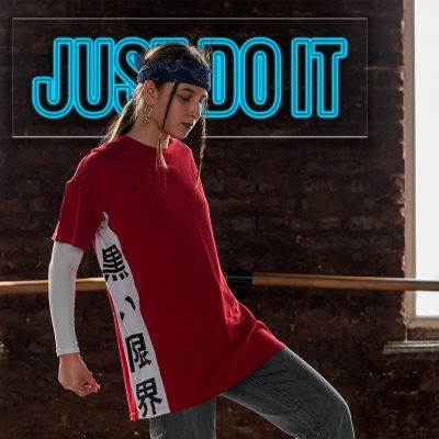 Mulher vestindo camisola vermelha desportiva com faixa branca e caracteres pretos, parede de tijolos e janelas ao fundo