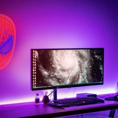 Configuração de escritório com monitor ultrapanorâmico, iluminação neon do Homem-Aranha e luz ambiente roxa