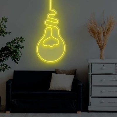 Sala com sofá preto, candeeiro de pé, luz de néon em forma de lâmpada e cómoda branca com planta e flores secas