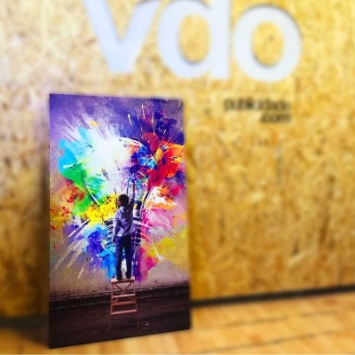 Caixa vertical com imagem colorida vibrante apoiada contra parede de madeira com letras VDO