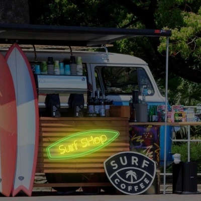 Carrinha quiosque de surf azul e branca com pranchas coloridas e sinais 'Surf Shop' e 'SURF COFFEE'