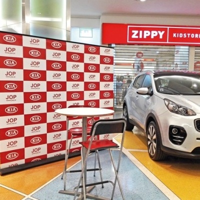 Carro branco KIA em exposição com painel de fundo e loja ZIPPY KIDSTORE